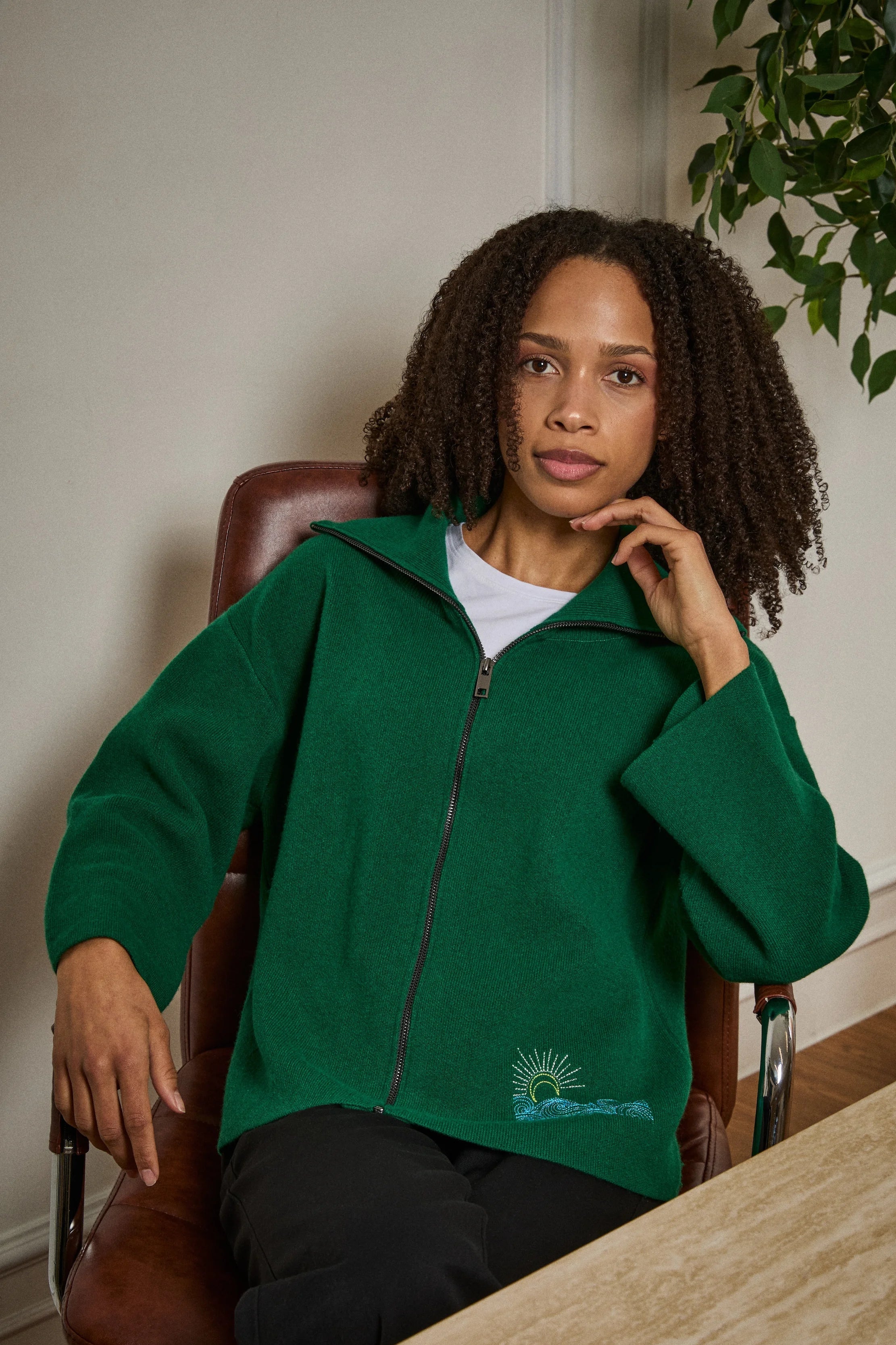 Woman wearing a green jacket with a logo, sitting in an office chair.